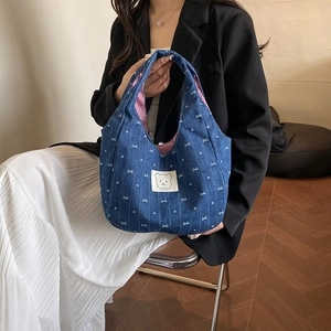 Blaue Denim-Einkaufstasche mit Herz-Schleifen-Muster und Bären-Aufnäher, stilvoll präsentiert