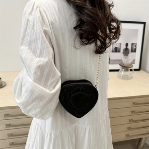 Quilted heart-shaped crossbody bag with gold chain strap worn by model in white dress