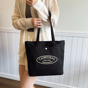 Large black canvas tote bag with front snap pocket and white logo for daily commute