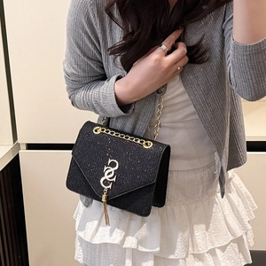Sac bandoulière noir scintillant à chaîne dorée et pompon porté par modèle