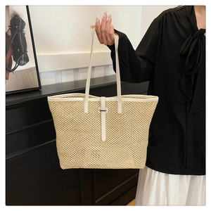 Detail of woven straw tote bag with white leather straps and metallic buckle ornament