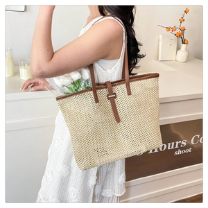 Detail of straw woven tote bag featuring brown leather trim and metallic buckle closure