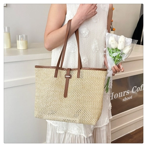 Detail of a beige woven straw tote bag with brown leather straps in a cozy setting