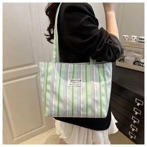 Macro detail of pleated stripe canvas tote bag featuring a green and blue fashion label