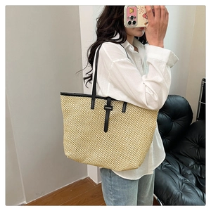 Detailed close-up of woven straw tote bag featuring black leather straps and texture