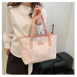 Detail showing pink textured tote bag with colorful wave embroidery and gold rivets
