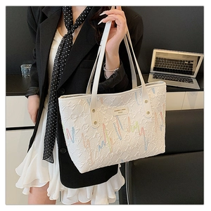 Detail of white quilted tote bag featuring wavy colorful embroidery and metal logo brand