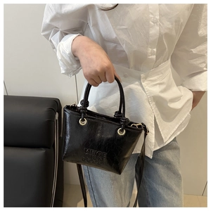 Close-up of black glossy leather tote bag with embossed letters and metal eyelet detail