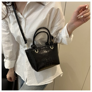Detail of black glossy patent leather bucket bag with embossed letter design and gold rings