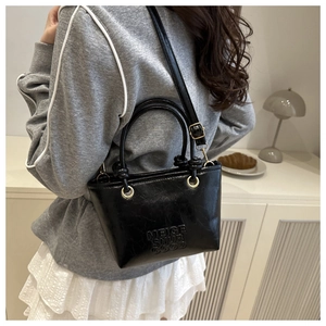 Model wearing a black glossy bucket bag with embossed text and gold hardware detail
