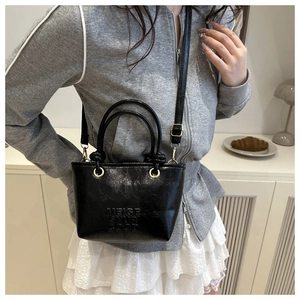 Detail of black mini bucket bag in glossy PU leather with debossed brand lettering