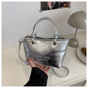 Detail of silver textured tote bag with embossed letters on a white aesthetic tabletop