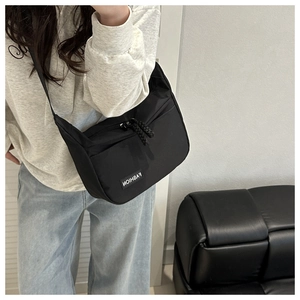 Close-up of black nylon crossbody bag with fashion label and woven rope zipper pull