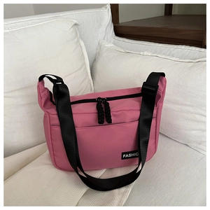 Detail of pink canvas crossbody bag with black wide strap and FASHIO label on a pillow