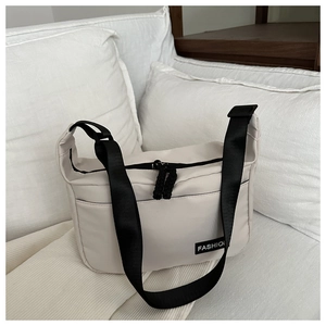 Detail of beige canvas crossbody bag featuring black adjustable strap and FASHION label