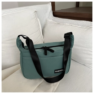 Detail of sage green nylon tote bag featuring adjustable black strap and fashion label