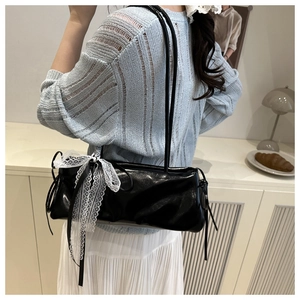 Détail d'un sac sous le bras noir brillant avec un nœud en dentelle blanche sur l'épaule
