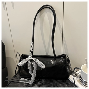 Detail of glossy black faux leather shoulder bag featuring a white lace bow decoration