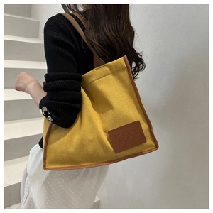 Detail of yellow corduroy tote bag featuring brown faux leather trim and woven shoulder strap