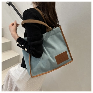 Detail of light blue waffle fabric tote bag with brown handles and fashion leather patch