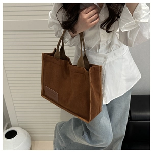 Detail of brown corduroy tote bag showing striped texture and faux leather brand patch