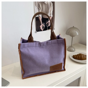 Close-up of purple corduroy tote bag featuring brown fabric straps and leather logo tag