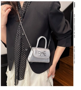 Détail du sac bandoulière argenté métallisé avec nœud porté sur un blazer noir