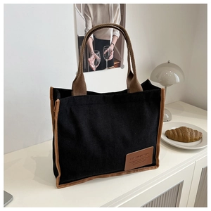 Detail of black corduroy tote bag featuring brown ribbon edges and leather fashion label