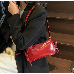 Dettaglio borsa baguette in pelle verniciata rossa con borchie argento e fiocchi laterali