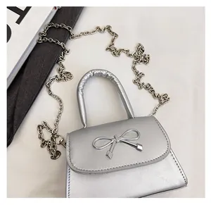 Detail view of the silver shiny handbag with a metallic bow and thin chain shoulder strap