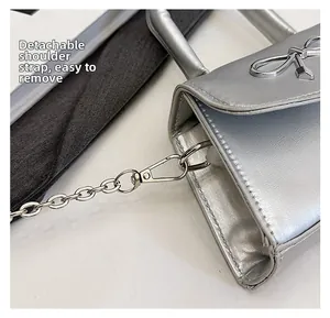 Detail of silver handbag featuring a metal bow clasp and detachable chain strap
