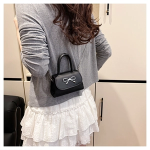 Détail d'un mini sac bandoulière noir avec un nœud argenté porté par un mannequin