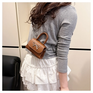 Petit sac à bandoulière marron avec nœud argenté porté par un mannequin pour l'été