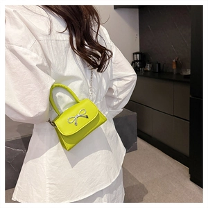 Detail of a neon green mini handbag with silver bow accent and metal chain strap