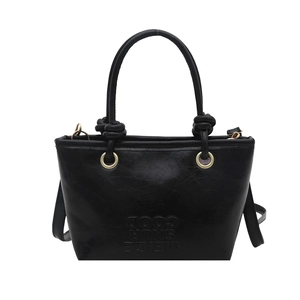 Minimalist black bucket bag with glossy texture and knot detail for 2025 fashion style