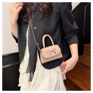 Mini crossbody bag with silver bow detail shown on a model on wooden stairs