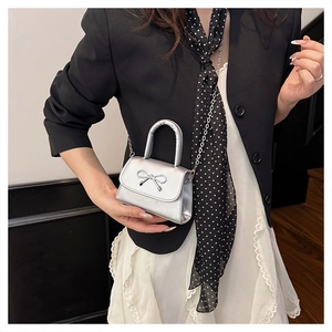 Close-up of a silver micro bag with bow detail and chain strap on a black blazer