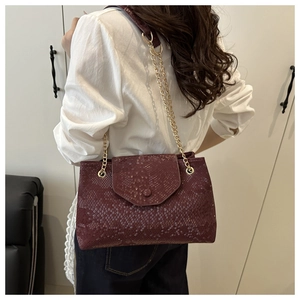 Burgundy snakeskin shoulder bag with gold chain strap worn by model in side profile