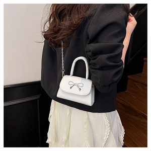 Close-up of mini white leather handbag with silver bow detail on a stylish woman