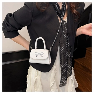 Close-up of white mini square bag with silver bow accent on a stylish model's outfit