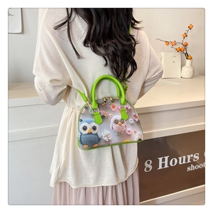 Detail of transparent shell bag with 3D knitted owl decor and green leather handle