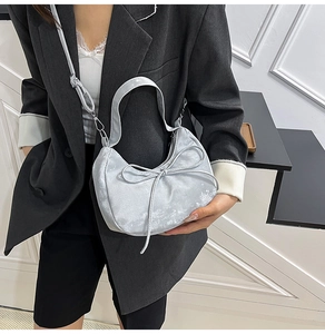 Detail of silver crescent bag featuring bow decoration and adjustable shoulder strap
