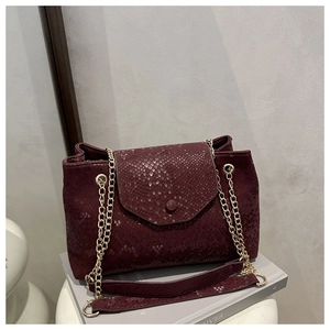 Detail of burgundy snakeskin textured handbag with gold chain strap and magnetic closure