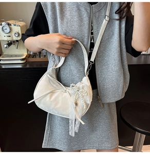 Detail of white hobo bag featuring matte leather texture and large lace bow with pearls