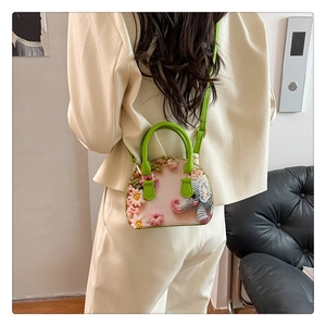 Detail of floral shell bag with 3D embroidery and green handles on a model