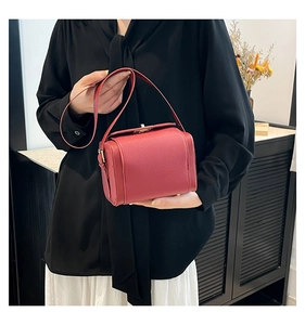 Detail of red box-style handbag with lychee pattern texture and top handle shown by model