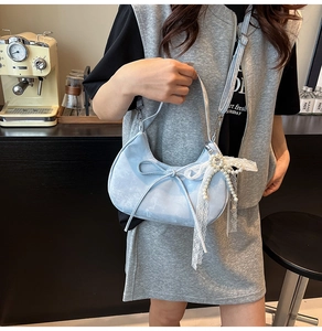 Detail of light blue crescent bag with matte texture, ribbon bow and pearl pendant charm
