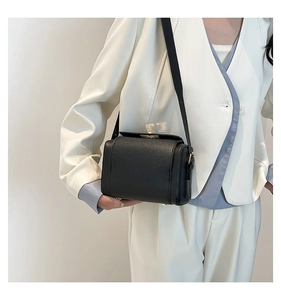Detail of black lychee grain leather box bag with gold metal clasp on white blazer