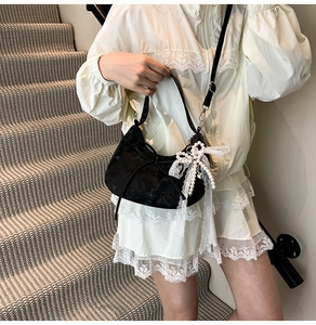 Detail view of black velvet dumpling bag with lace bow and pearl charm worn by model