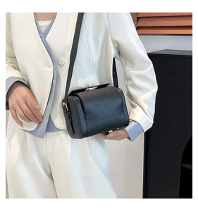 Close-up of black litchi leather vintage crossbody bag with gold metal lock on white blazer
